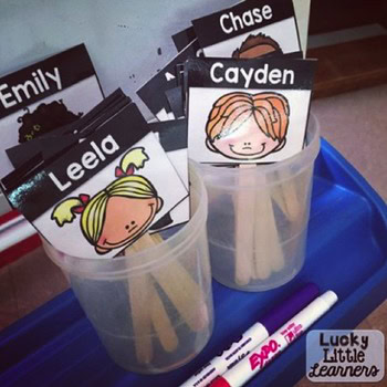 A colorful display of editable mini name tag labels with illustrated children's faces and names, organized in clear containers on a blue tray, perfect for classroom name tags and student organization.