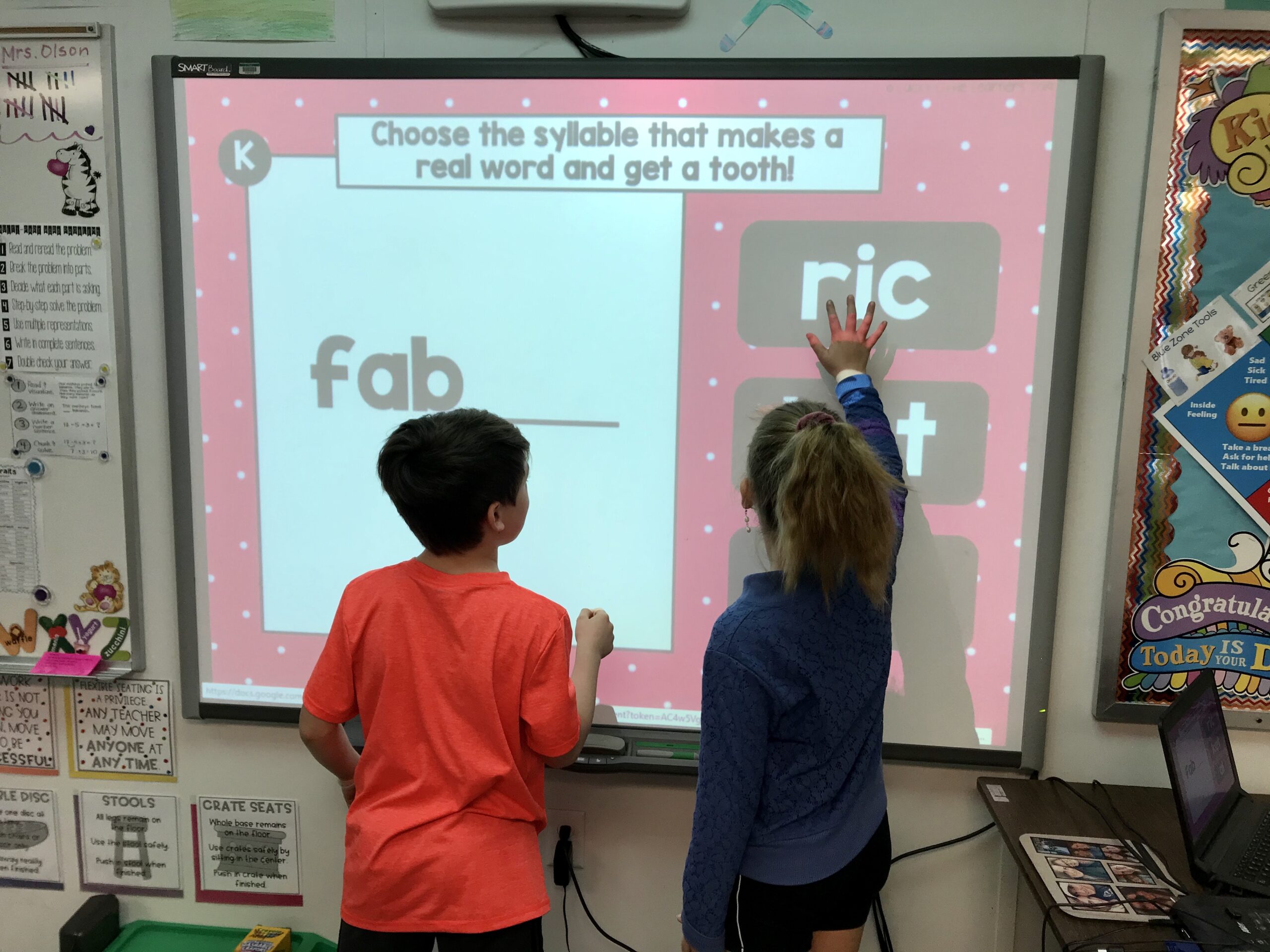 Choose the syllable that makes a real word and get a tooth! Children interact with a digital game on a classroom smartboard, focusing on multisyllabic words from the Toothy® Pack.