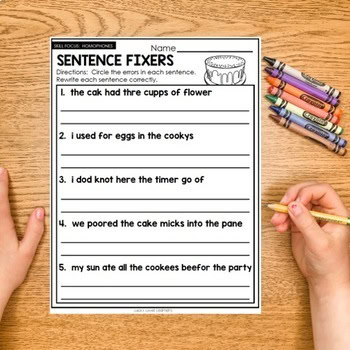 Sentence Fixers #2 worksheet for improving sentence structure and grammar skills, featuring colorful markers and a student's hand writing on a wooden desk.